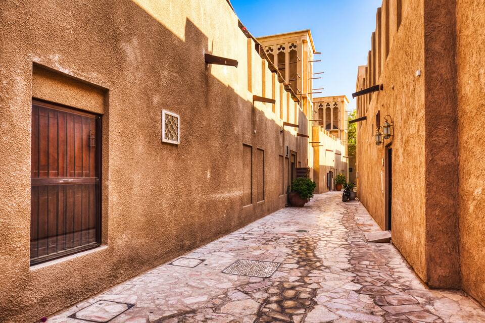 A narrow cobblestone street flanked by buildings with textured walls and wooden doors.
