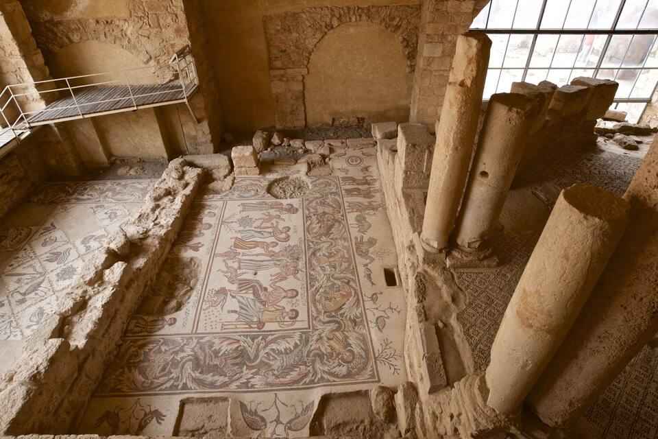 Um antigo chão de mosaico com desenhos intrincados, colunas de pedra e um guarda-corpo de metal.