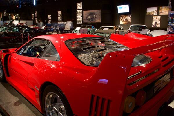 Une voiture de sport rouge, dotée d’un aileron arrière et dont les éléments du moteur sont visibles, exposée dans un salon.