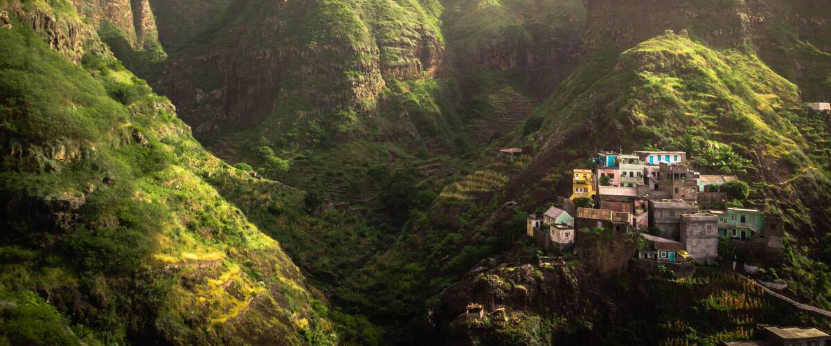 A mountainous landscape with terraced fields and a cluster of colorful buildings perched on a cliff.