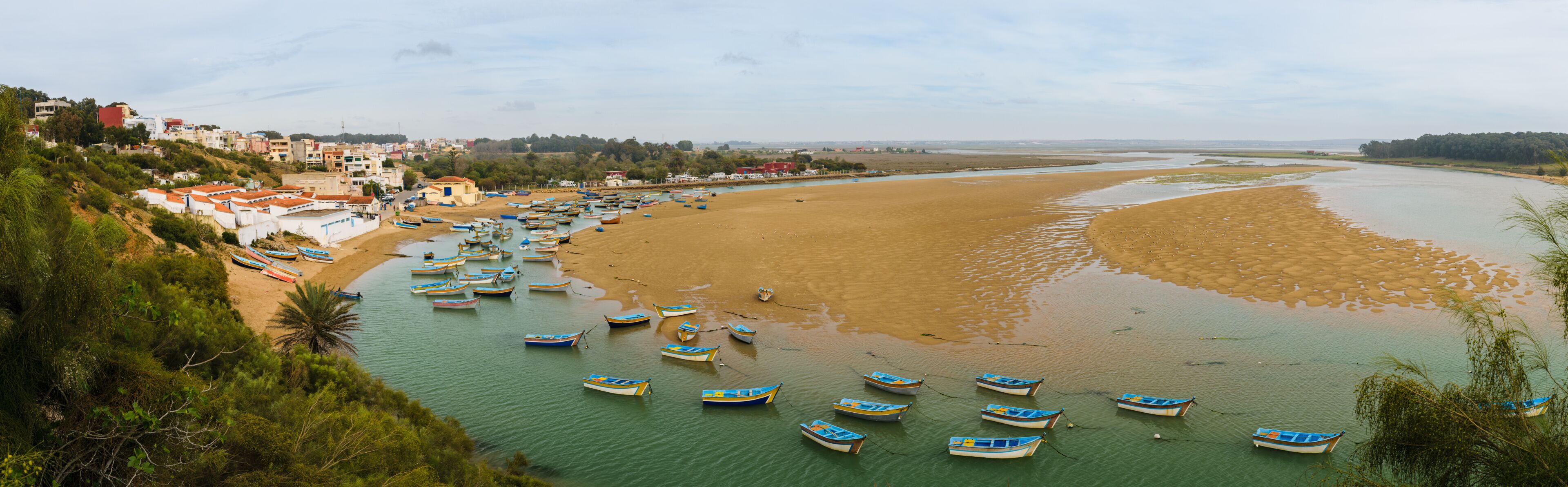 A coastal town with boats on a sandy beach and a river.