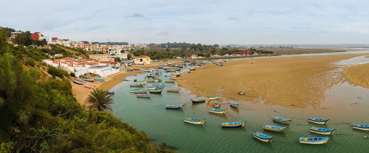 A coastal town with boats on a sandy beach and a river.