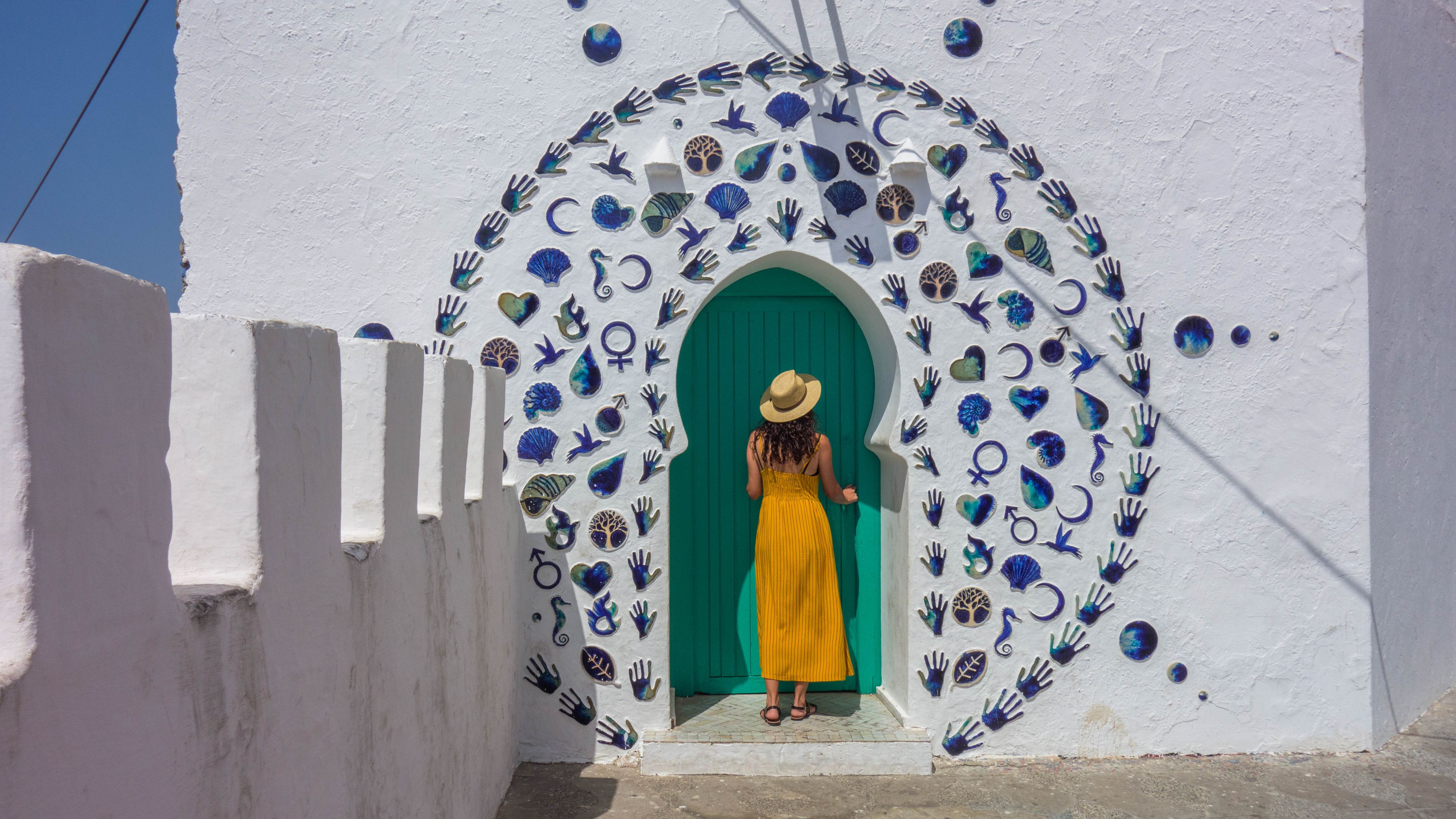 Woman in yellow dress and hat in a nice decorated door of the village of Asilah in Morocco