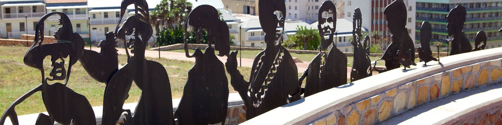 A metal sculpture of musicians on a stone wall with a cityscape in the background.