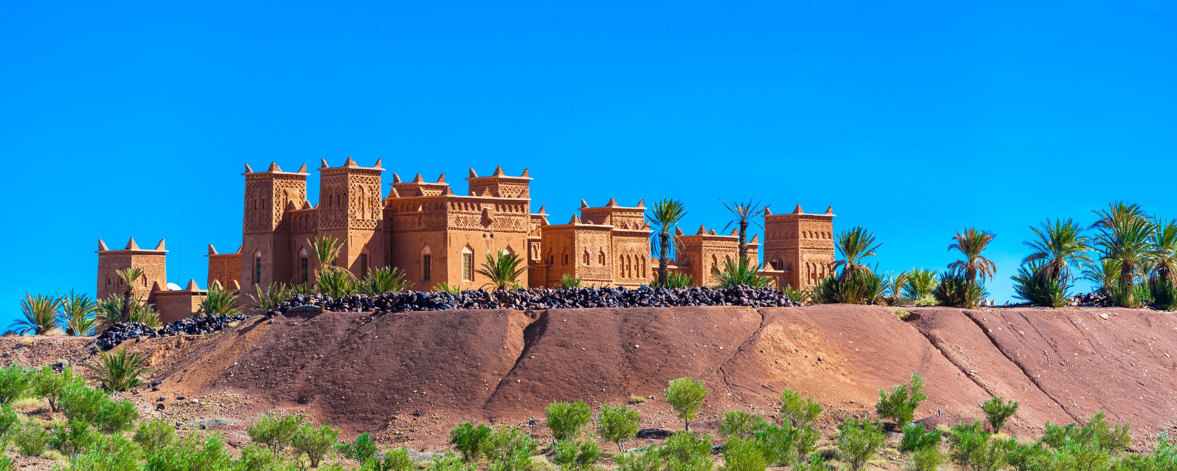 A large, ornate building with multiple towers and arches, situated on a rocky hill with sparse vegetation.