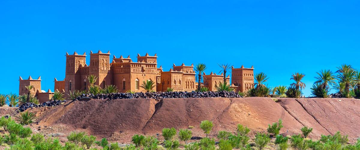 A large, ornate building with multiple towers and arches, situated on a rocky hill with sparse vegetation.