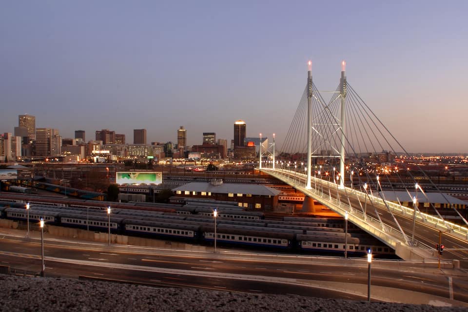 Ein Stadtpanorama im Abendlicht mit einer markanten Schrägseilbrücke und mehreren Gleisen.