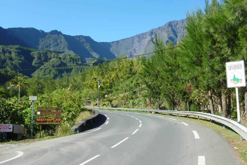 Uma estrada sinuosa com guarda-corpo, cercada por vegetação exuberante e montanhas.
