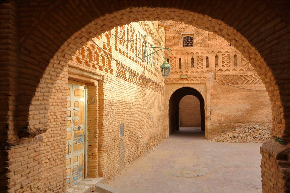 An arched passageway with brick walls, a door, and a lantern.