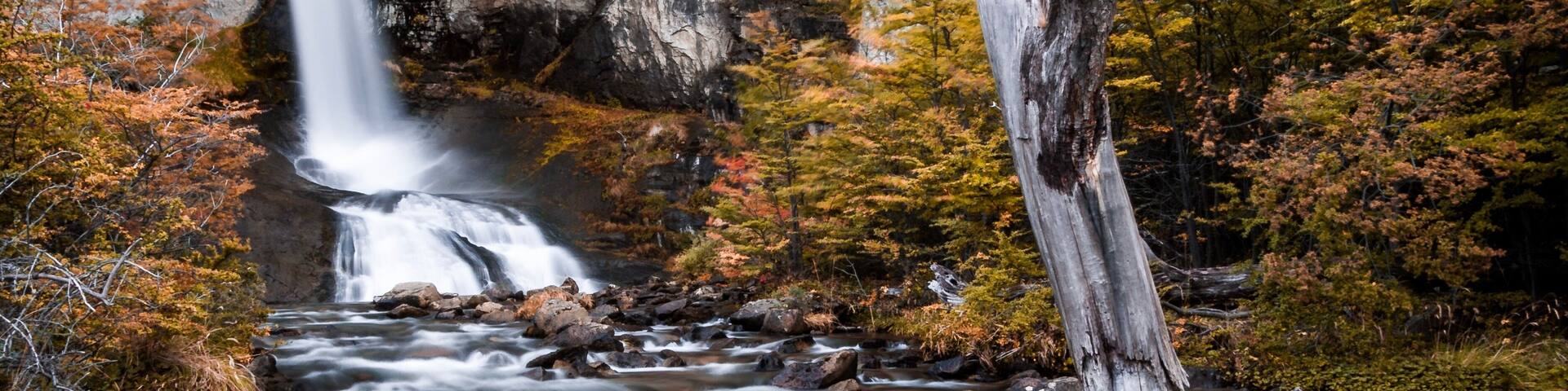 Una cascada que se precipita en un río, rodeado de follaje otoñal y acantilados rocosos.