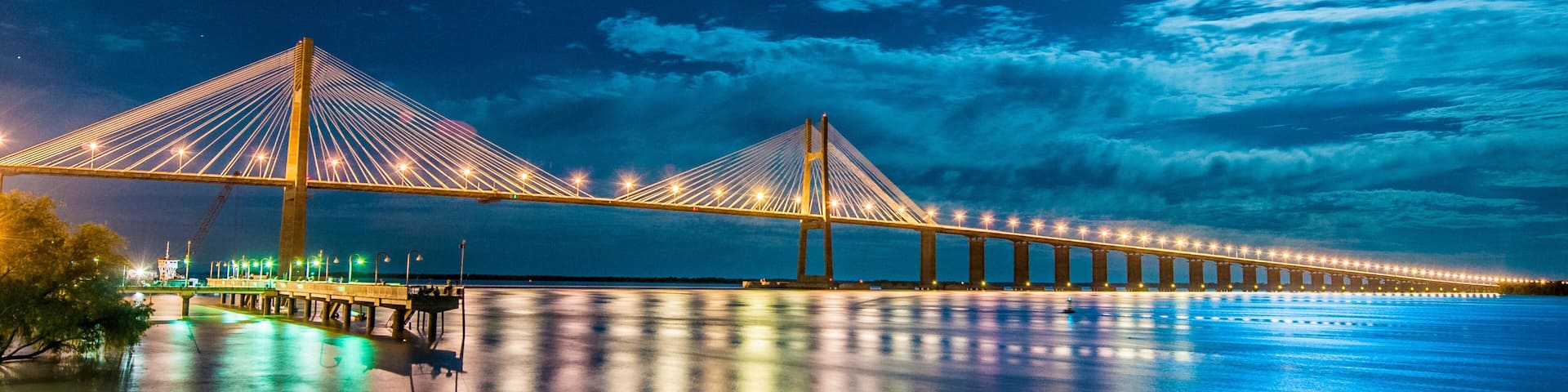 A long suspension bridge at night with lights reflecting on the water.