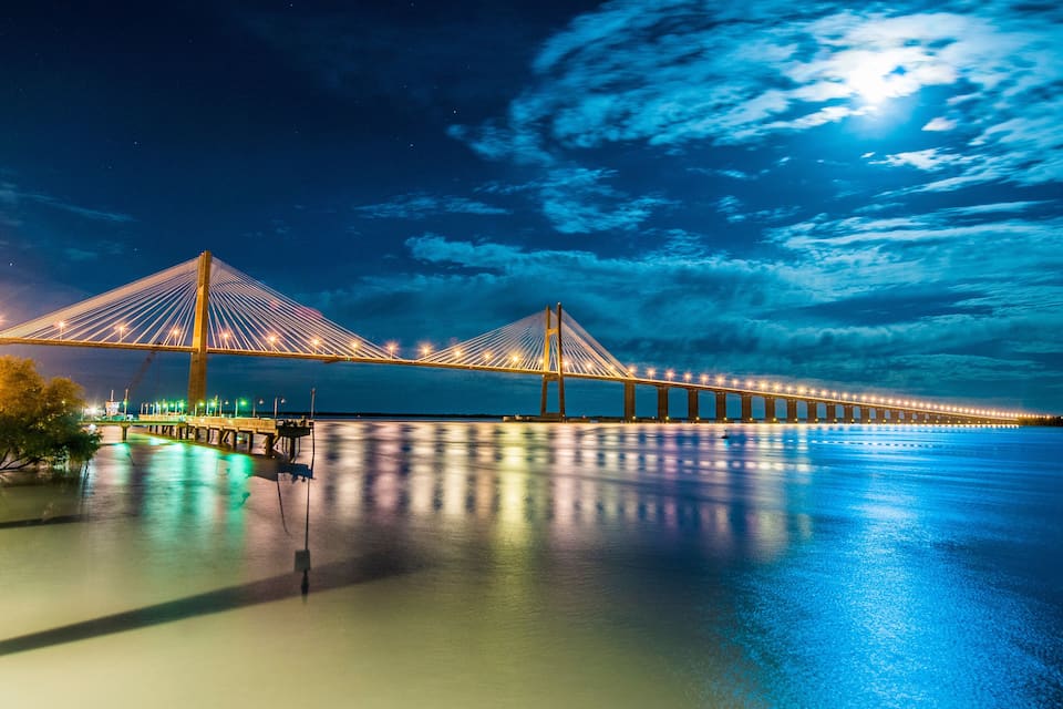 A long suspension bridge at night with lights reflecting on the water.