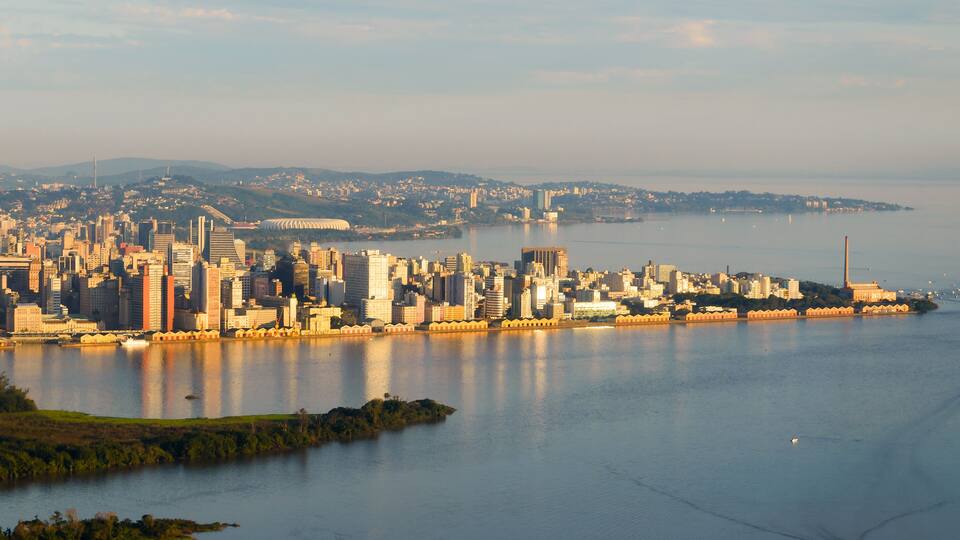 A coastal cityscape with a prominent skyline, a large body of water, and distant hills.