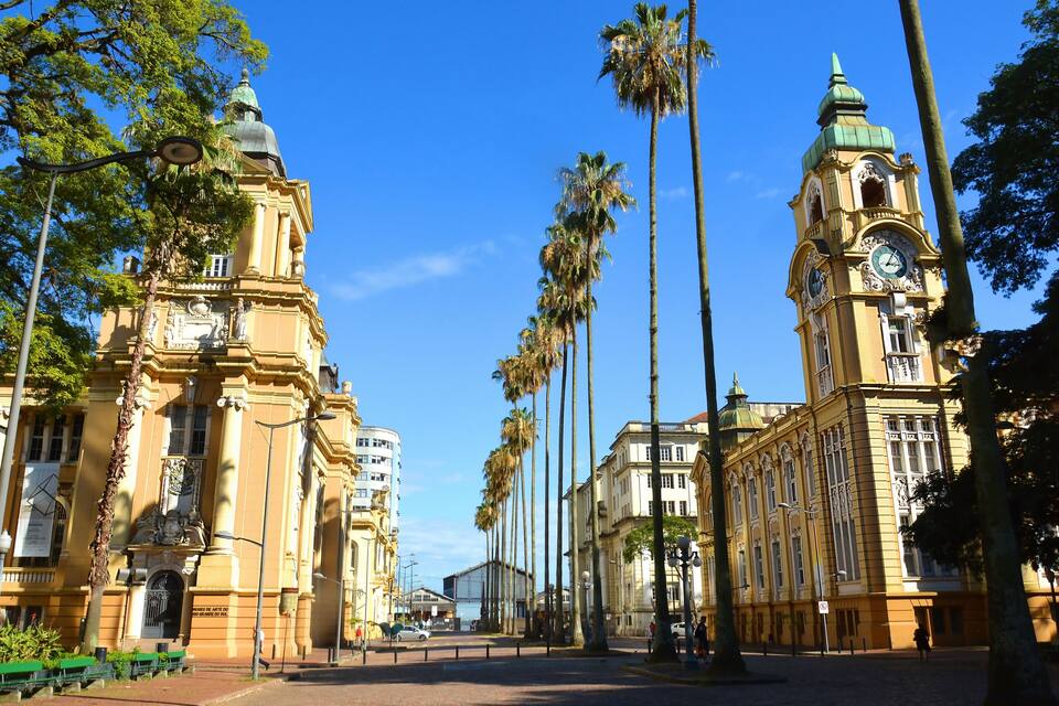 A street lined with palm trees and historic buildings with clock towers.