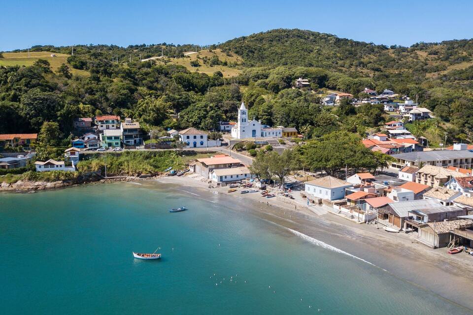 Uma vila costeira com uma igreja imponente, uma praia e colinas ao redor.