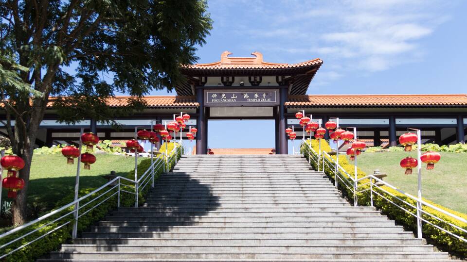 A temple entrance with a traditional roof, stairs leading up to it, and red lanterns.