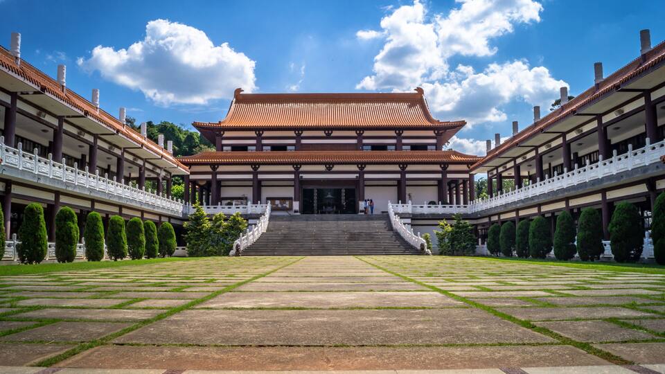 A traditional building with a tiled roof, surrounded by a symmetrical garden with neatly trimmed hedges and a central pathway leading to the entrance.