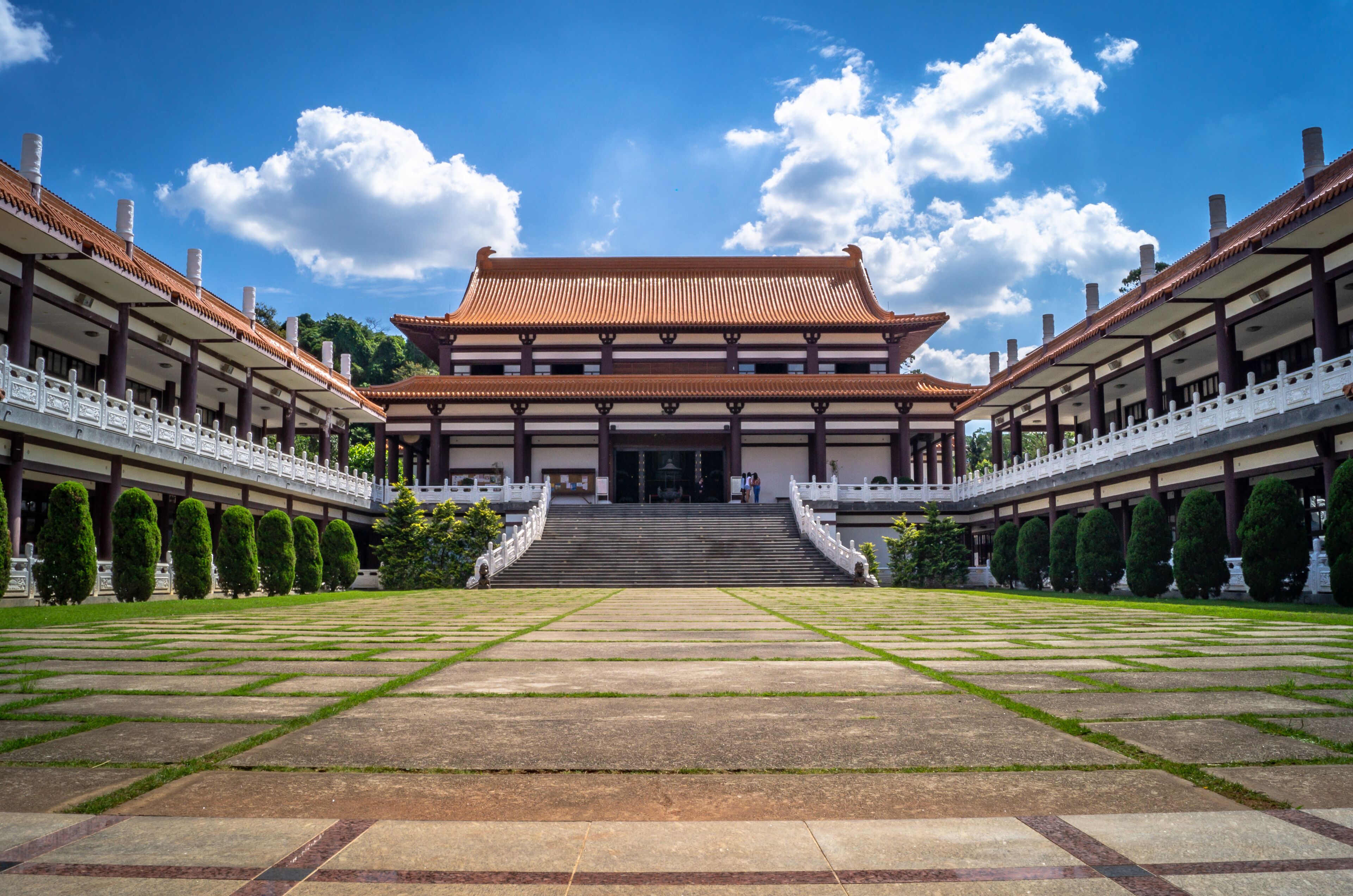 A traditional building with a tiled roof, surrounded by a symmetrical garden with neatly trimmed hedges and a central pathway leading to the entrance.
