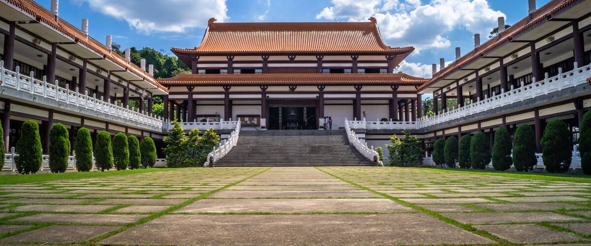 A traditional building with a tiled roof, surrounded by a symmetrical garden with neatly trimmed hedges and a central pathway leading to the entrance.