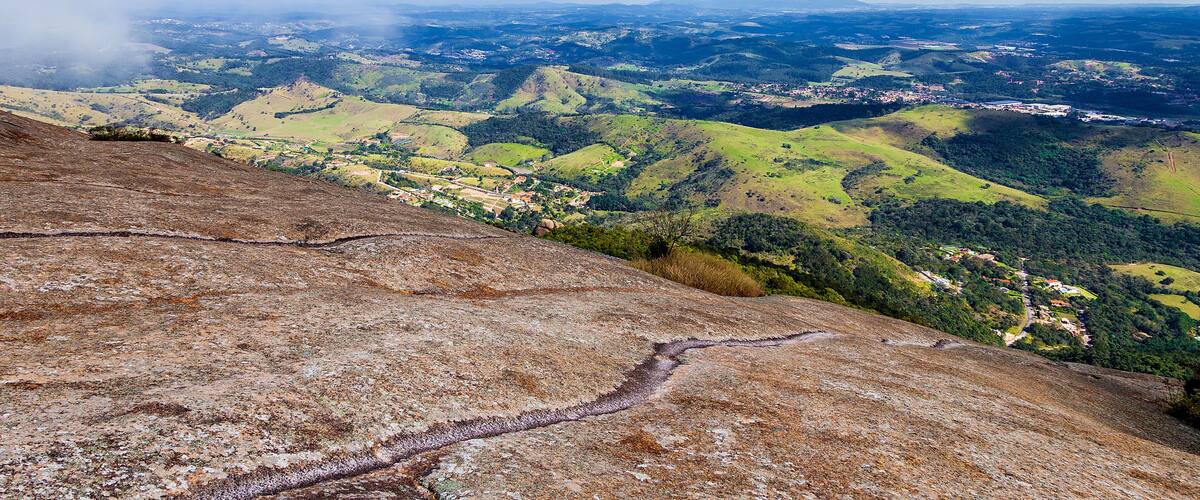 A panoramic view of a hilly landscape with a winding path, lush green valleys, and distant towns.