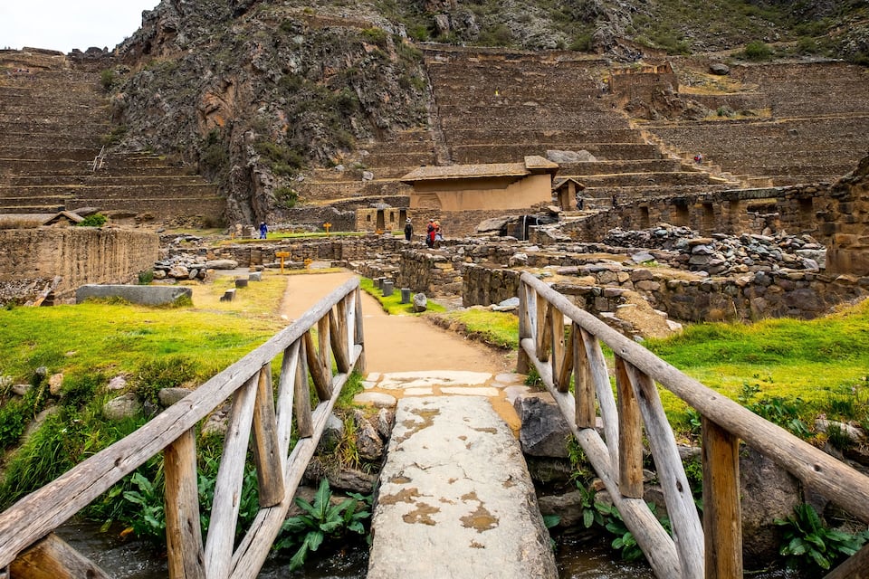 A stone bridge leading to ancient ruins with terraced steps and a large rock formation.