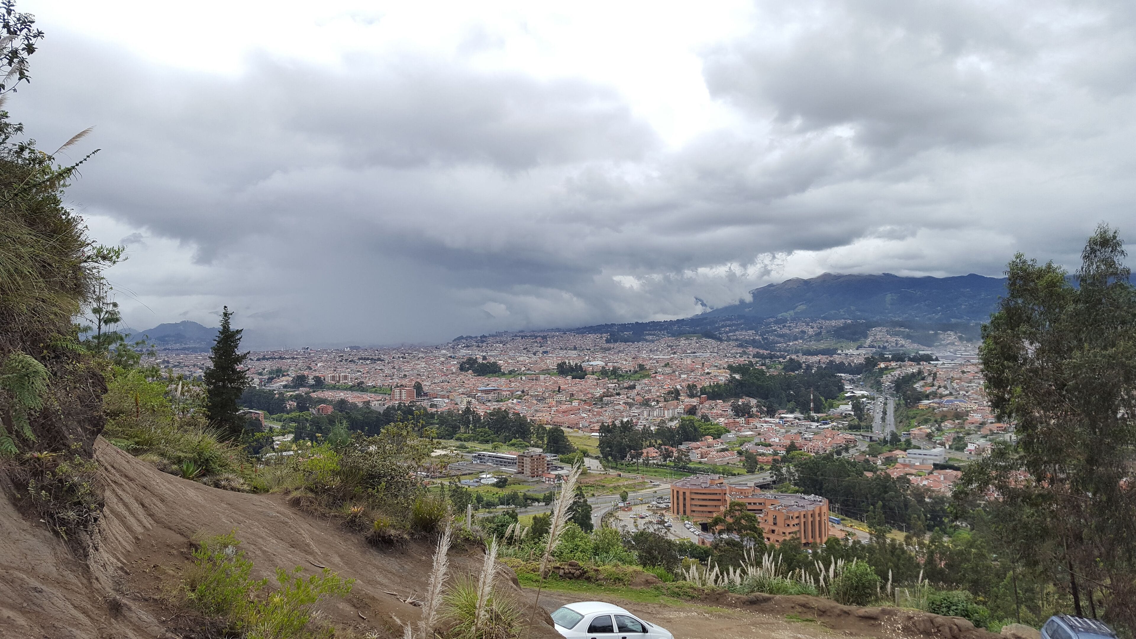A cityscape with a mountainous backdrop under cloudy skies.