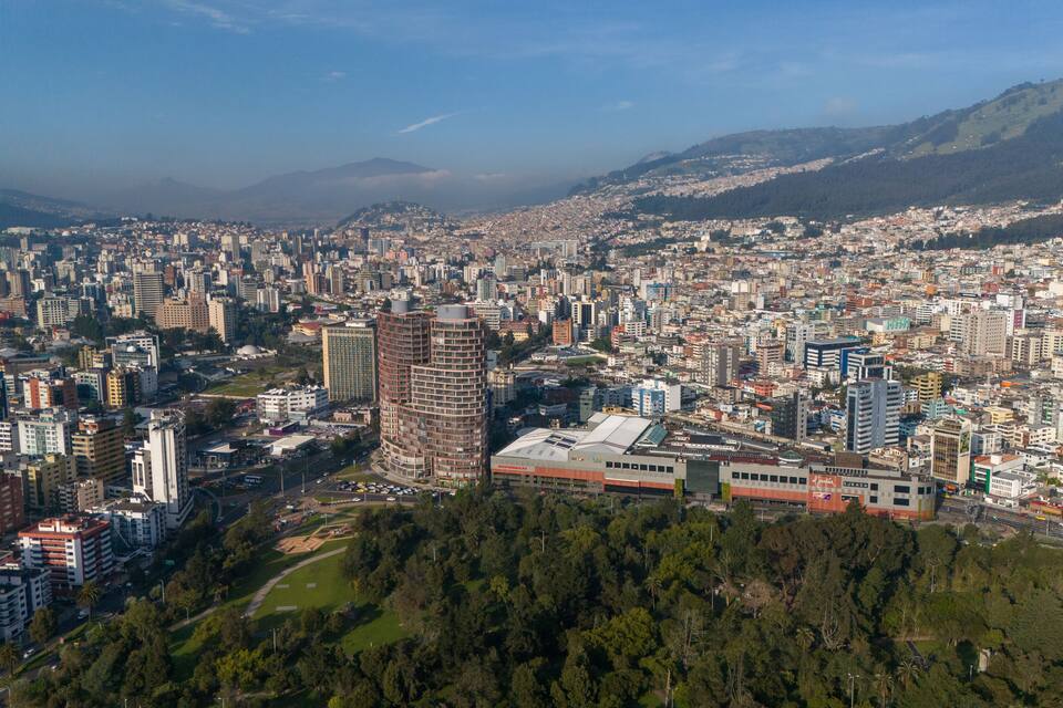 Un paisaje urbano denso con numerosos rascacielos, una estación de tren destacada y montañas al fondo.