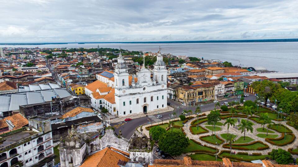 A coastal cityscape with a prominent white church, a circular garden, and a view of the sea.