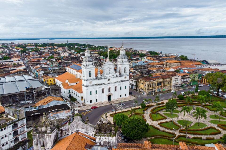 Un paisaje urbano costero con una iglesia blanca destacada, un jardín circular y vista al mar.