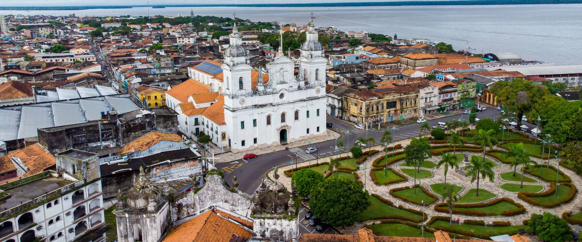 A coastal cityscape with a prominent white church, a circular garden, and a view of the sea.