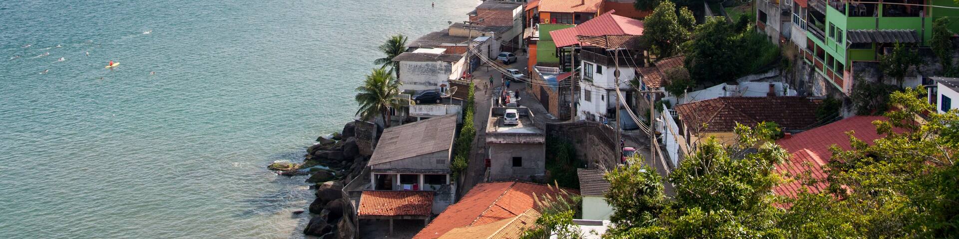 A coastal town with a beach, colorful buildings, and mountains in the background.