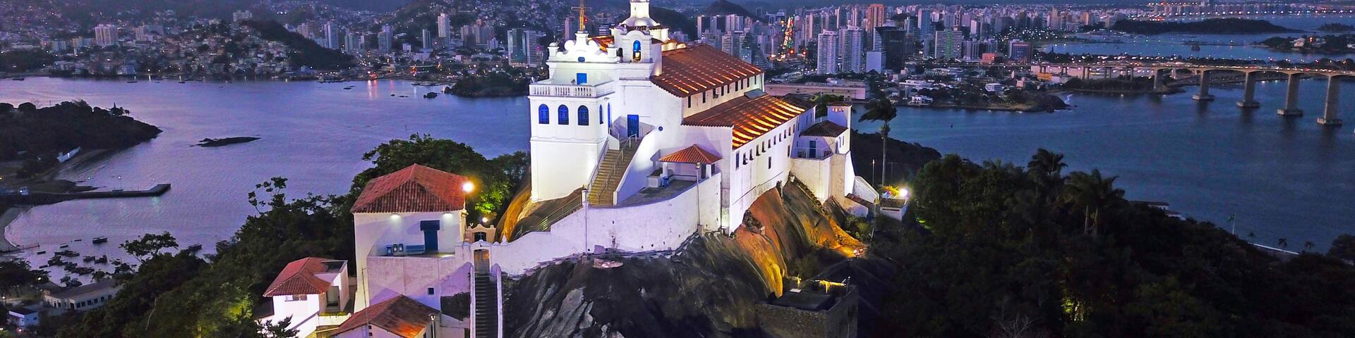 A white church with a bell tower on a hill overlooking a city and a river.