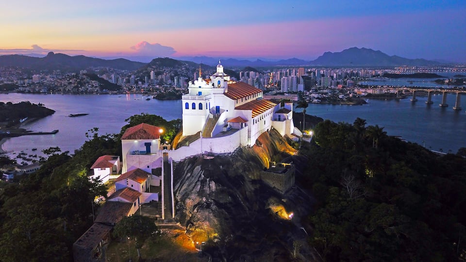A white church with a bell tower on a hill overlooking a city and a river.