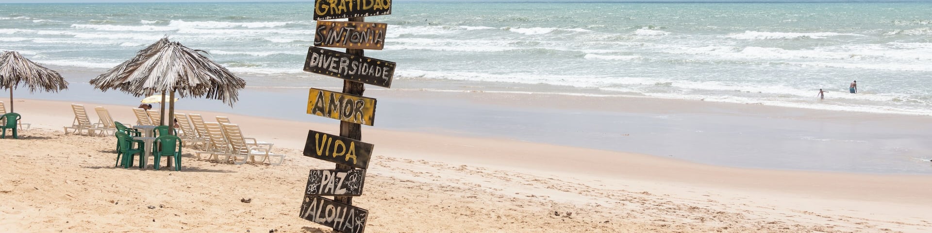 Una playa con un letrero de madera que enumera palabras como 'Gratidão' y 'Vida'.
