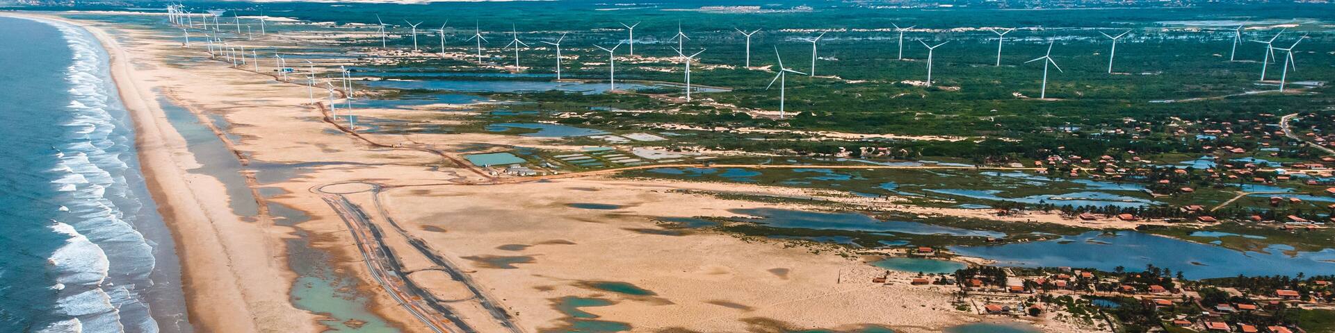 An aerial view of a coastal area with wind turbines, a beach, and a small settlement.