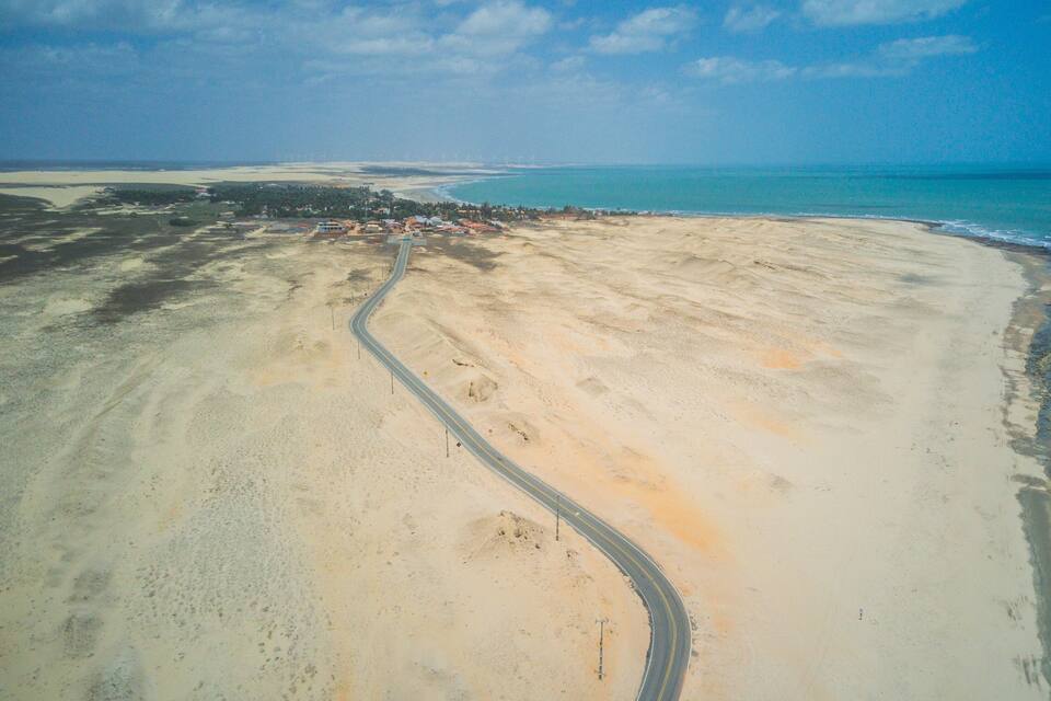 En kustväg som slingrar sig genom ett sandigt landskap, med en strand på ena sidan och en klarblå himmel ovanför.