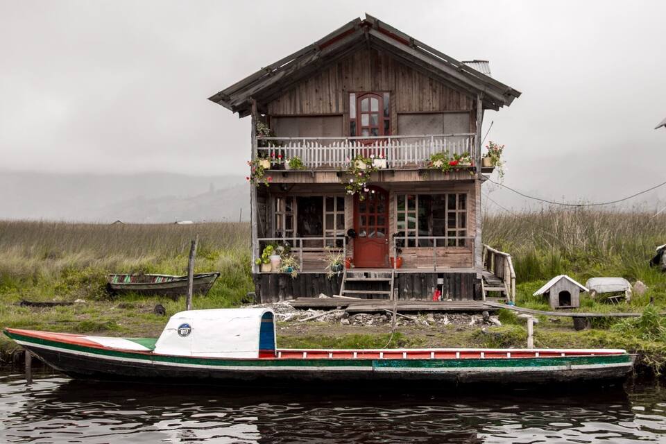 A wooden house with a balcony, surrounded by water and vegetation.