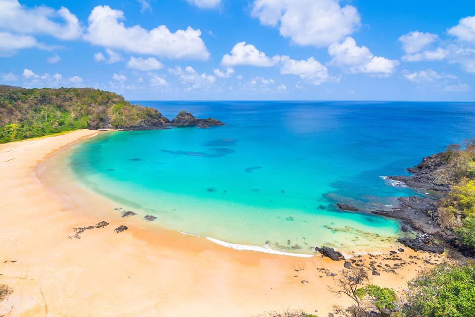 Une plage tropicale aux eaux turquoise et limpides, bordée de sable fin et ponctuée de formations rocheuses.