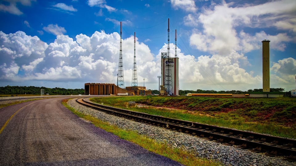 A railway track curving through a landscape with industrial structures, including tall towers and a cylindrical building.