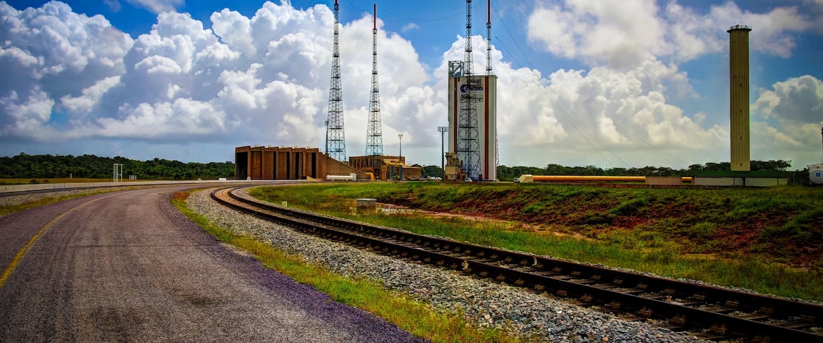 A railway track curving through a landscape with industrial structures, including tall towers and a cylindrical building.
