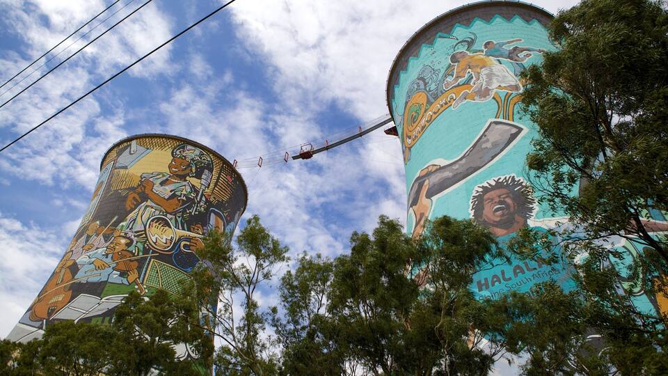 Dois grandes murais em estruturas cilíndricas com arte vibrante retratando cenas culturais e a palavra "Malaka".