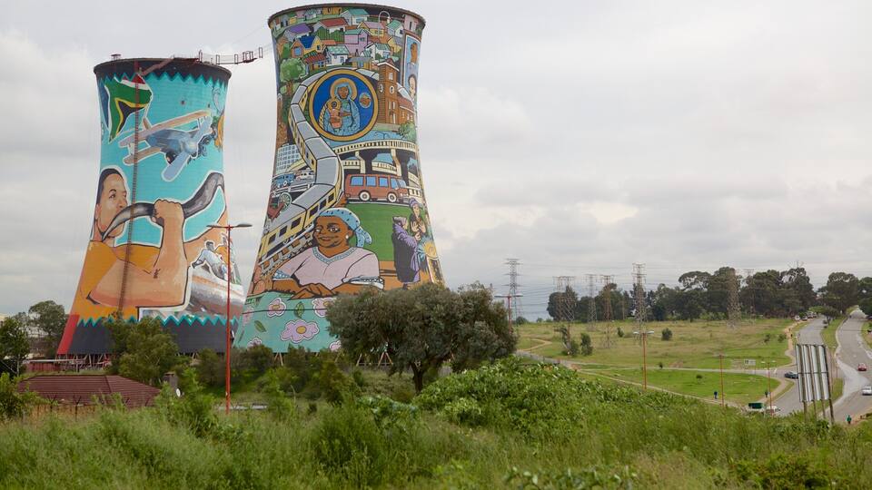 Duas grandes torres de água com murais coloridos, uma estrada e linhas de energia ao fundo.