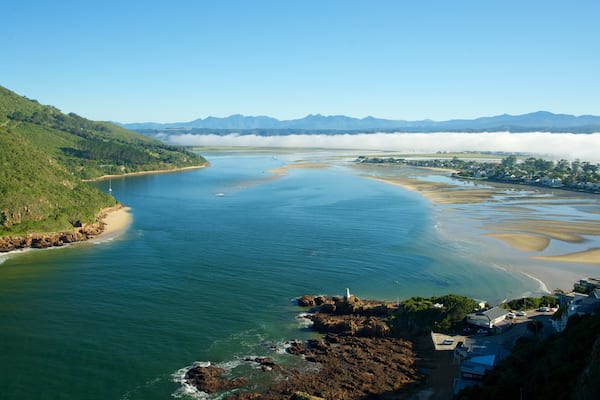 Paisagem costeira com rio, margem rochosa e um farol.