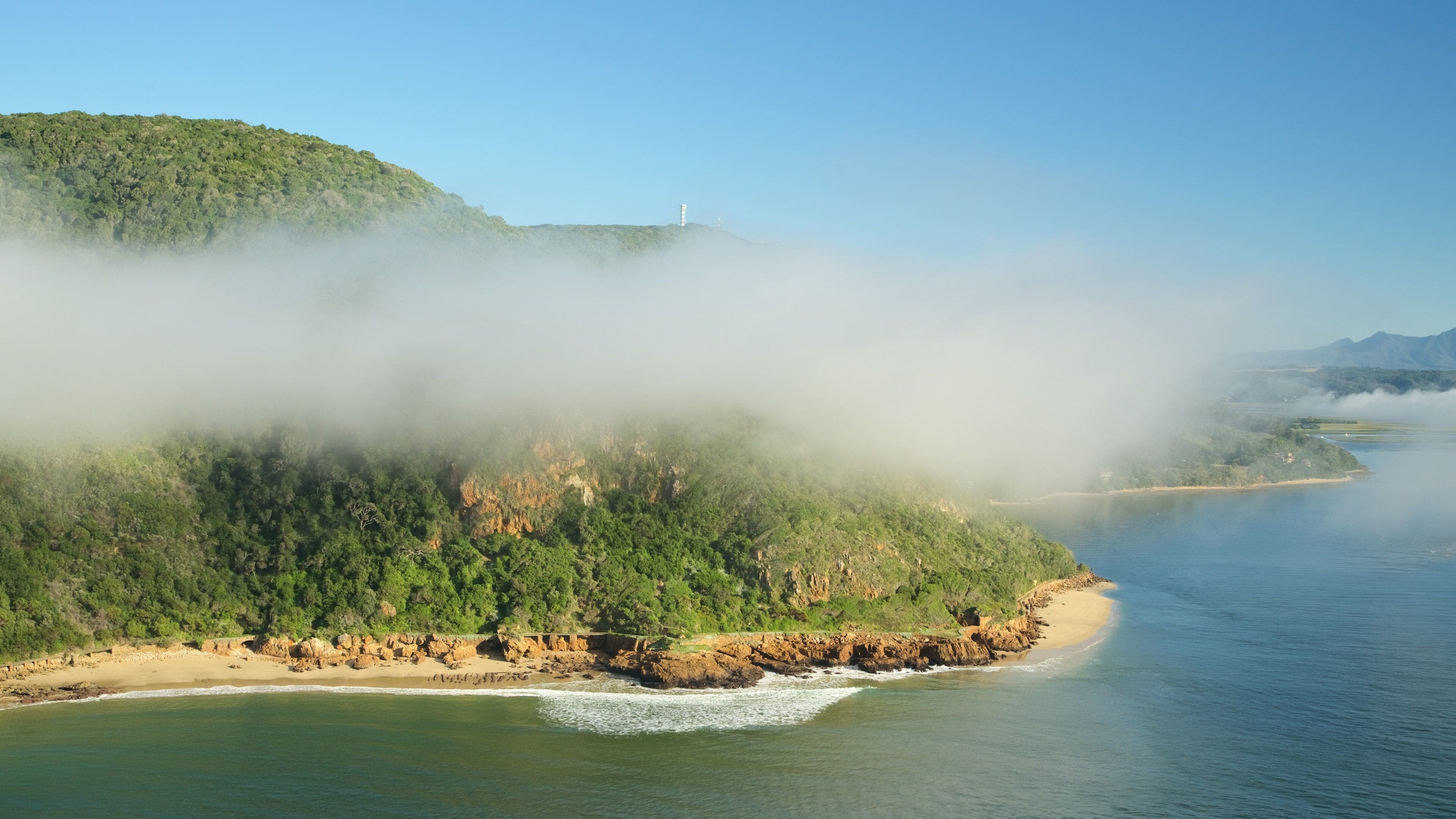 A coastal landscape with a beach, rocky cliffs, and a lighthouse.