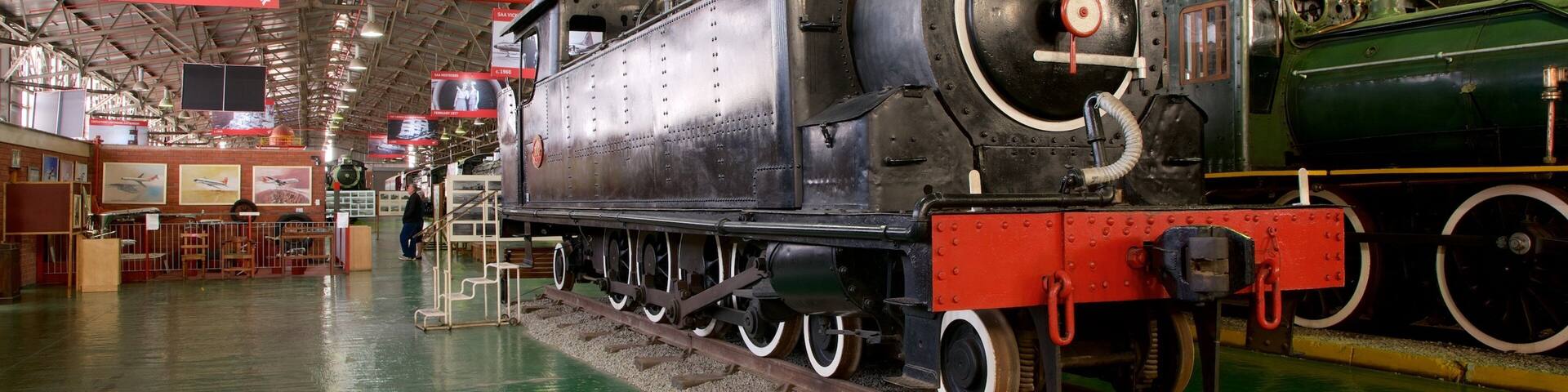 A large steam locomotive in a museum with a green floor and red tracks.
