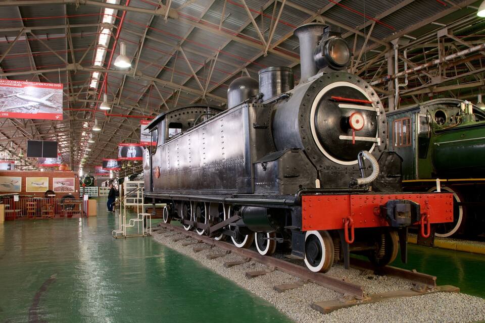 Una gran locomotora a vapor en un museu, amb un paviment verd i vies vermelles.