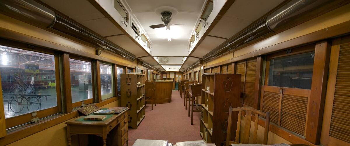 A train car with wooden desks and chairs, books, and papers.