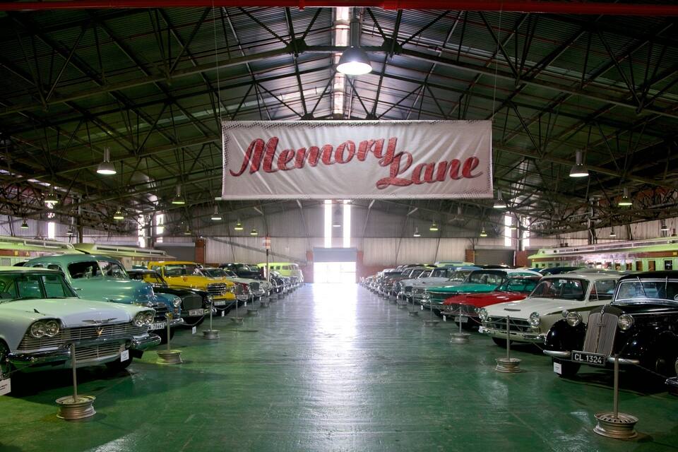 Exposición de autos antiguos con un cartel que dice 'Avenida de la Memoria'.