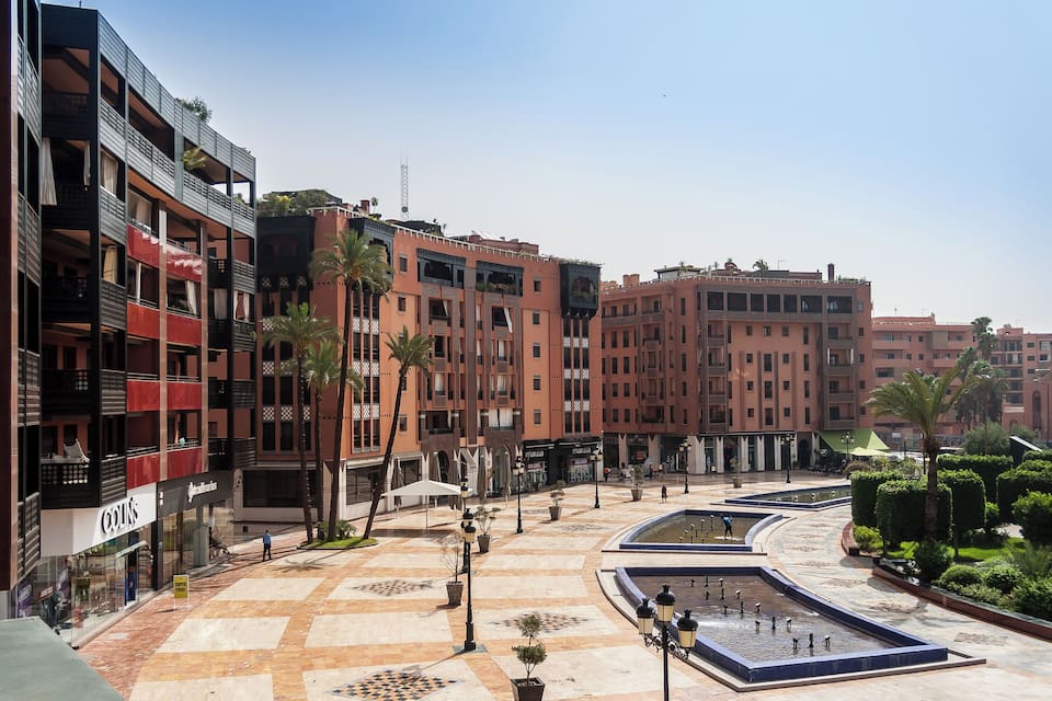 A courtyard with a fountain, palm trees, and modern buildings with balconies.