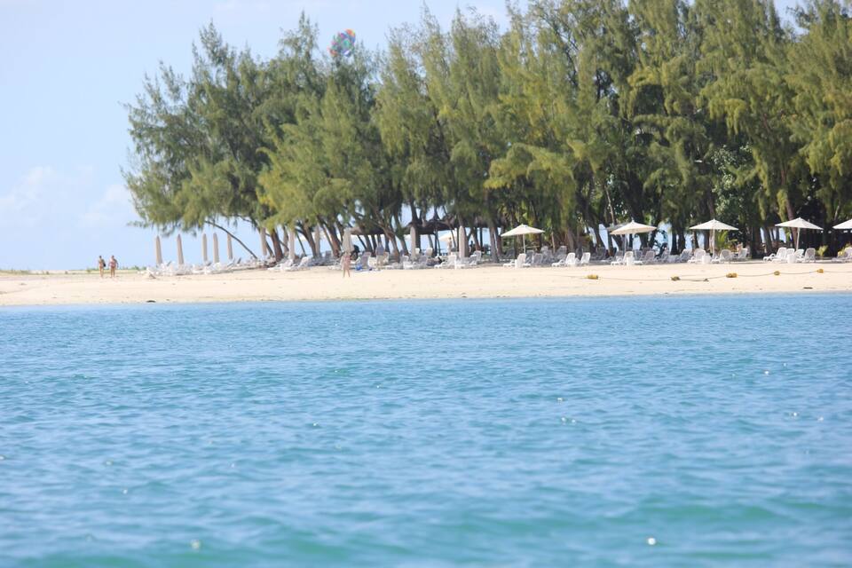 A beach with white sand, clear blue water, and rows of white umbrellas and lounge chairs.